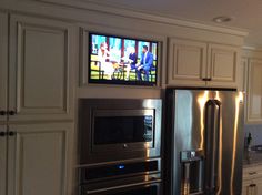 a large stainless steel refrigerator in a kitchen with two televisions on the wall above it