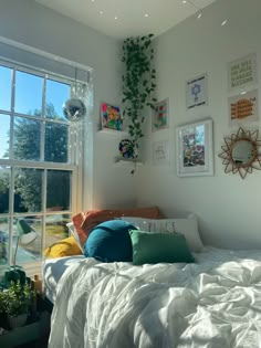 a bed with white sheets and pillows in front of a large window filled with plants