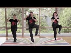 two people are doing yoga in front of large windows, one person is standing on the floor