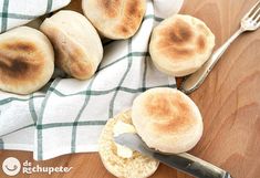 bread rolls with butter spread on them sitting next to a knife and fork, on a wooden table