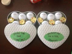 two heart shaped boxes filled with golf balls on top of a table next to candy