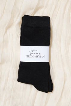 two pairs of black socks sitting on top of a white bed sheet with the word groomsman written across it