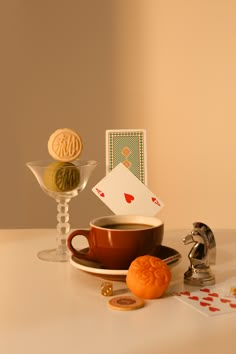 a cup of tea, playing cards and a cookie are sitting on a white table