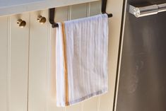 a white towel hanging on the side of a kitchen cabinet with brass handles and knobs