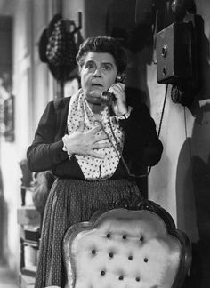 an old black and white photo of a woman talking on the phone while sitting in a chair