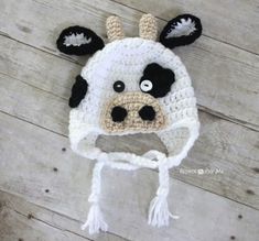 a crocheted cow hat with black eyes and ears on top of a wooden floor