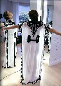 a woman standing in front of a mirror holding her arms out to the side while wearing a white and black dress