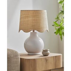 a white lamp sitting on top of a wooden table next to a potted plant