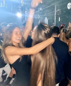 two young women dancing at a party with their arms around each other in the air