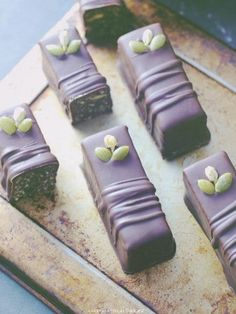 chocolate bars with pistachios on top sit on a cutting board next to a knife