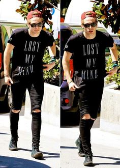 the man is walking down the street in his t - shirt and ripped jeans,