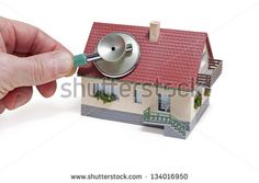 a hand holding a magnifying glass over a small house with a red roof