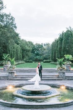 a bride and groom standing in front of a fountain at the end of their wedding day