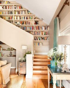 a living room filled with lots of furniture and bookshelves next to a stair case