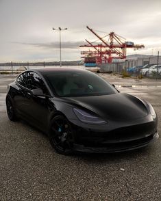 a black tesla parked in a parking lot next to a construction site with cranes behind it