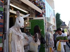 a woman standing next to a white bunny in front of a store filled with people