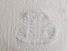 a drawing of a cake on top of a white table cloth with blue thread and crayons