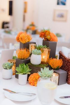 an arrangement of succulents and candles on a white table cloth with place settings