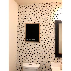 a white toilet sitting under a bathroom mirror next to a black and white polka dot wall