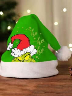 a green and white santa hat with the grinch on it's side sitting next to a christmas tree