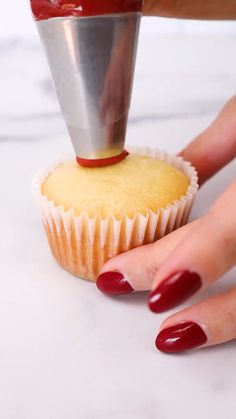 a woman's hand reaching for a cupcake with red nail polish on it