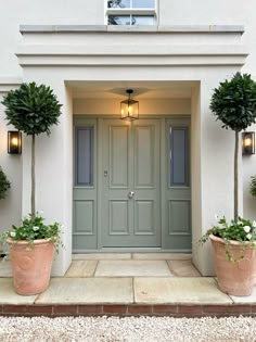 two potted plants are in front of the door of a white house with green doors