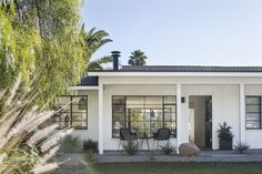 a small white house with two chairs in the front yard and palm trees behind it