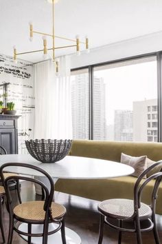 a dining room table with chairs and a couch in front of a large window overlooking the city