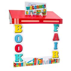 a red table topped with lots of colorful magnets next to a welcome book sign