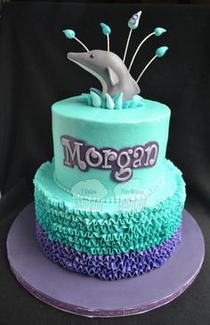 a blue and purple cake with a dolphin on it's top that says morgan