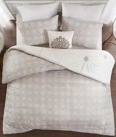 a bed with white comforters and pillows on top of the headboard in front of a window