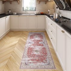 a kitchen with white cabinets and wooden floors, an area rug in the middle of the floor