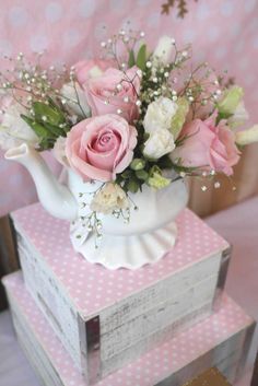 a white tea pot with pink roses and baby's breath in it on top of two stacked boxes