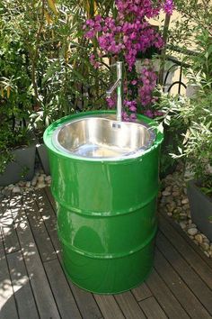 a large green barrel sitting on top of a wooden deck next to plants and flowers