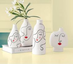 three white vases with faces painted on them sitting next to a book and flower