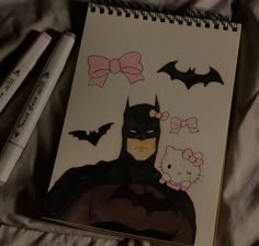 a drawing of batman and hello kitty on top of a bed next to two markers