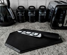 a kitchen counter topped with black appliances and coffee pots next to a cutting board that has a knife on it