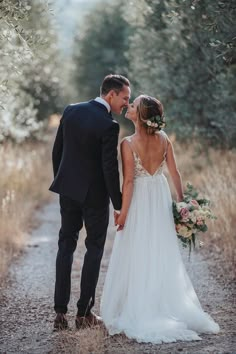 a bride and groom kissing in the middle of an olive tree lined path at their wedding