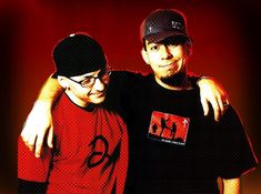 two men standing next to each other in front of a red wall with one holding his arm around the other's shoulder