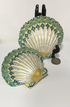 two green and gold fan shaped dishes sitting on top of a white table next to a coin