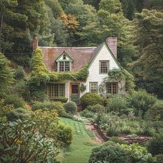 a house surrounded by lush green trees and shrubbery in the foreground is a garden