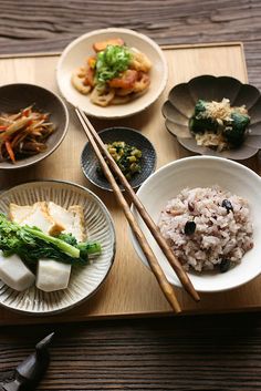 a wooden tray topped with bowls filled with rice and veggies next to chopsticks