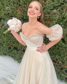 a woman in a white dress is holding flowers and posing for the camera with her hands on her hips