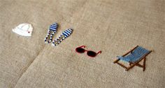 a chair, sunglasses and hat are on the ground next to a beach towel that has been embroidered onto it