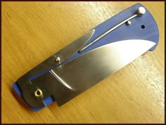 a blue and silver knife sitting on top of a wooden table next to a pair of scissors