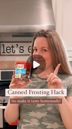 a woman holding a jar of canned frosting in her hand and pointing to the camera