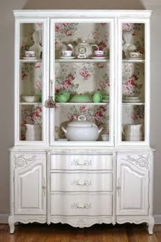 a white china cabinet with floral wallpaper