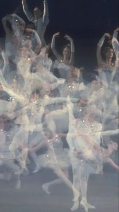 a large group of ballet dancers in white outfits and tutus, all with their arms raised