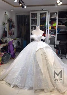 a white wedding dress on display in a room with lots of clothes and other items