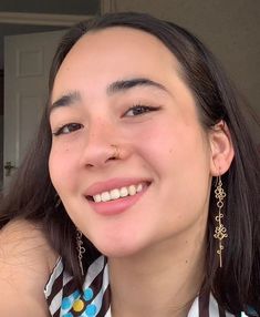 a woman with long dark hair wearing earrings and smiling at the camera while looking to her left